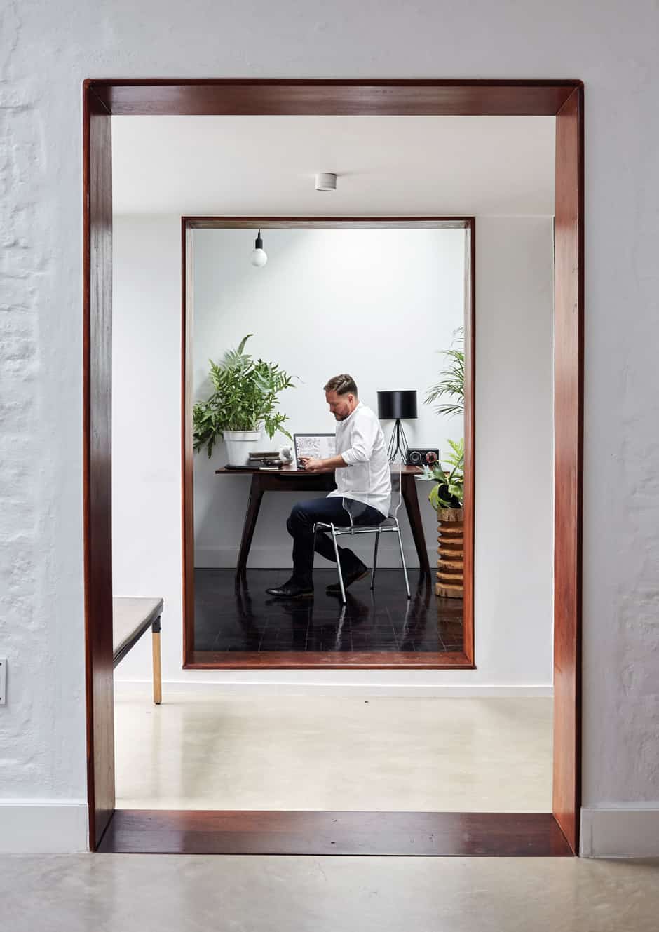 OFFICE Christo is pictured in the entry vestibule connecting the main house to the study, which creates a frame for the vintage desk, the lightness of the composition maintained by a transparent polycarbonate chair. Indoor plants bring an organic element to the clean-lined simplicity of the white, cube-like space, lit from above by skylights. The floor in this area is parquet salvaged from the rest of the house. 